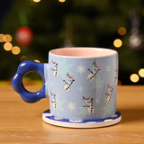 Blue porcelain Frozen Snowman mug with scalloped ring handle and pink interior, printed with Olaf, snowflakes and stars, set on a matching round coaster.