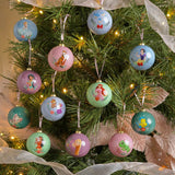Set of 12 round glossy baubles in muted blue, pink and green tones, each printed with a Disney princess or sidekick design, shown hanging on a decorated Christmas tree.