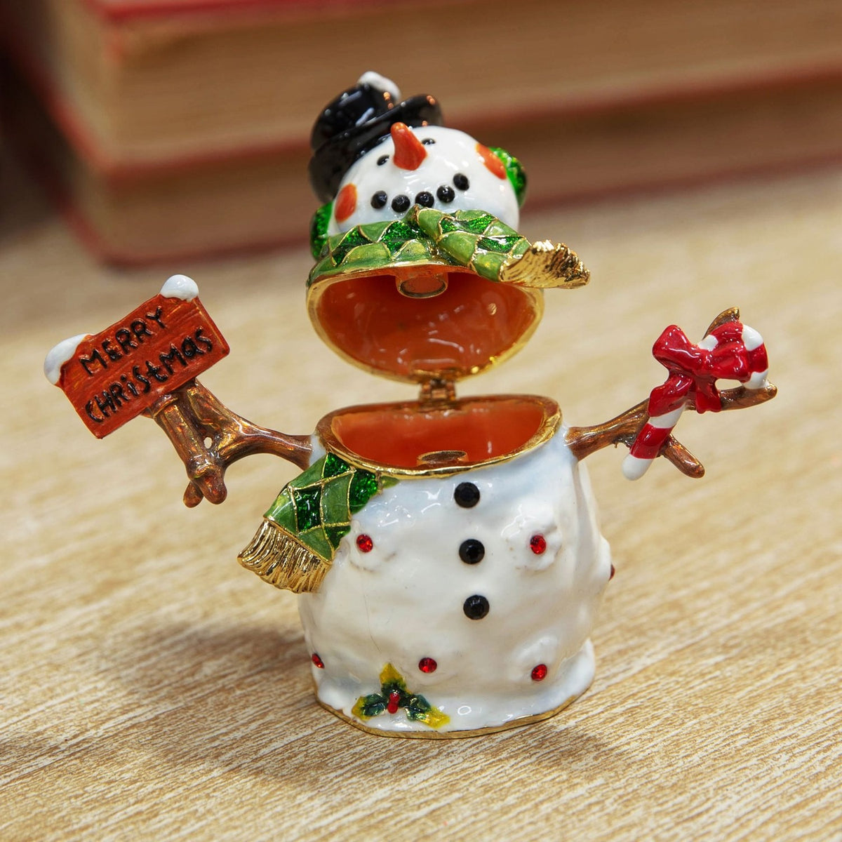 Christmas Snowman Metal Trinket Box with hinged lid open, white glossy finish, black top hat, green scarf, holding a Merry Christmas sign and candy cane, on a wooden surface.