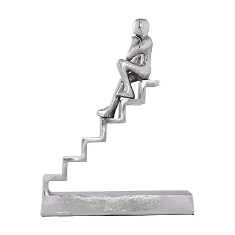 Zadiwin Figurine in nickel-finish aluminium, a seated figure resting chin on hand atop a diagonal staircase on a rectangular base, shown on a plain white background.