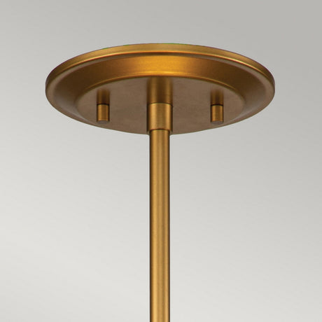 A close-up of the Ziggy 2 Light Duo-Mount Medium Pendant/Semi-Flush in lacquered gold highlights its contemporary design with a ceiling canopy and rod. The round plate at the top features a smooth, matte finish and an adjustable rod for customizable height. The background is plain and light gray.