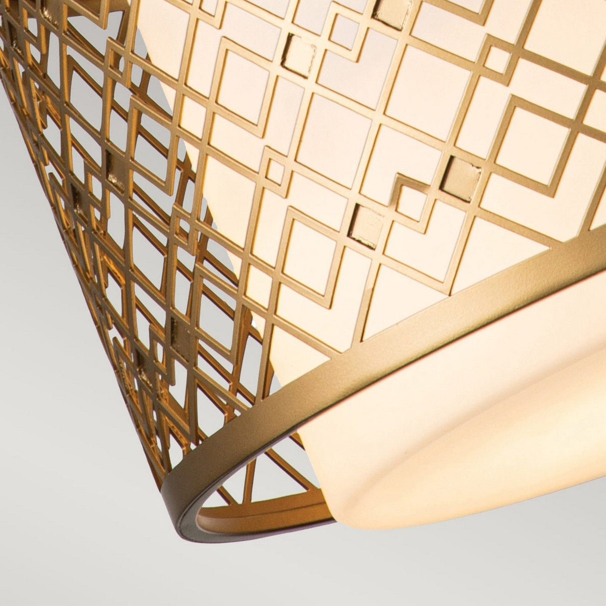Close-up of the Ziggy 2 Light Duo-Mount Medium Pendant/Semi-Flush in Lacquered Gold, showcasing its modern lampshade with a geometric lattice pattern. The warm glow from within highlights the intricate square and rectangular designs against a plain background. Its contemporary style ensures it fits seamlessly into any stylish setting.