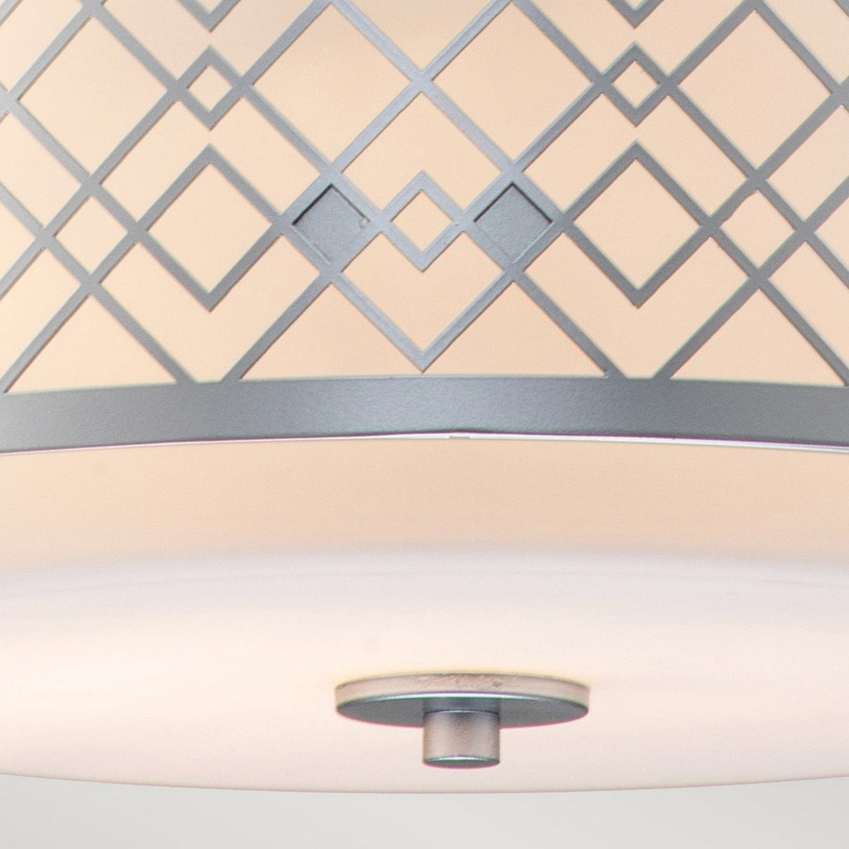 A close-up of the Ziggy 2 Light Duo-Mount Medium Pendant/Semi-Flush in Lacquered Silver highlights its adaptable lighting and geometric pattern. The crisscrossing lines form diamond shapes on the shade, which is attached to a circular base. The neutral and soft colors enhance its modern, contemporary design for an elegant appearance.