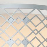 A close-up view of the Ziggy 2 Light Medium Flush showcases its geometric metal lattice pattern with interlocking diamond shapes, finished in lacquered silver. The light gray structure stands out against an off-white background, creating a striking contrast between the foreground and background elements.
