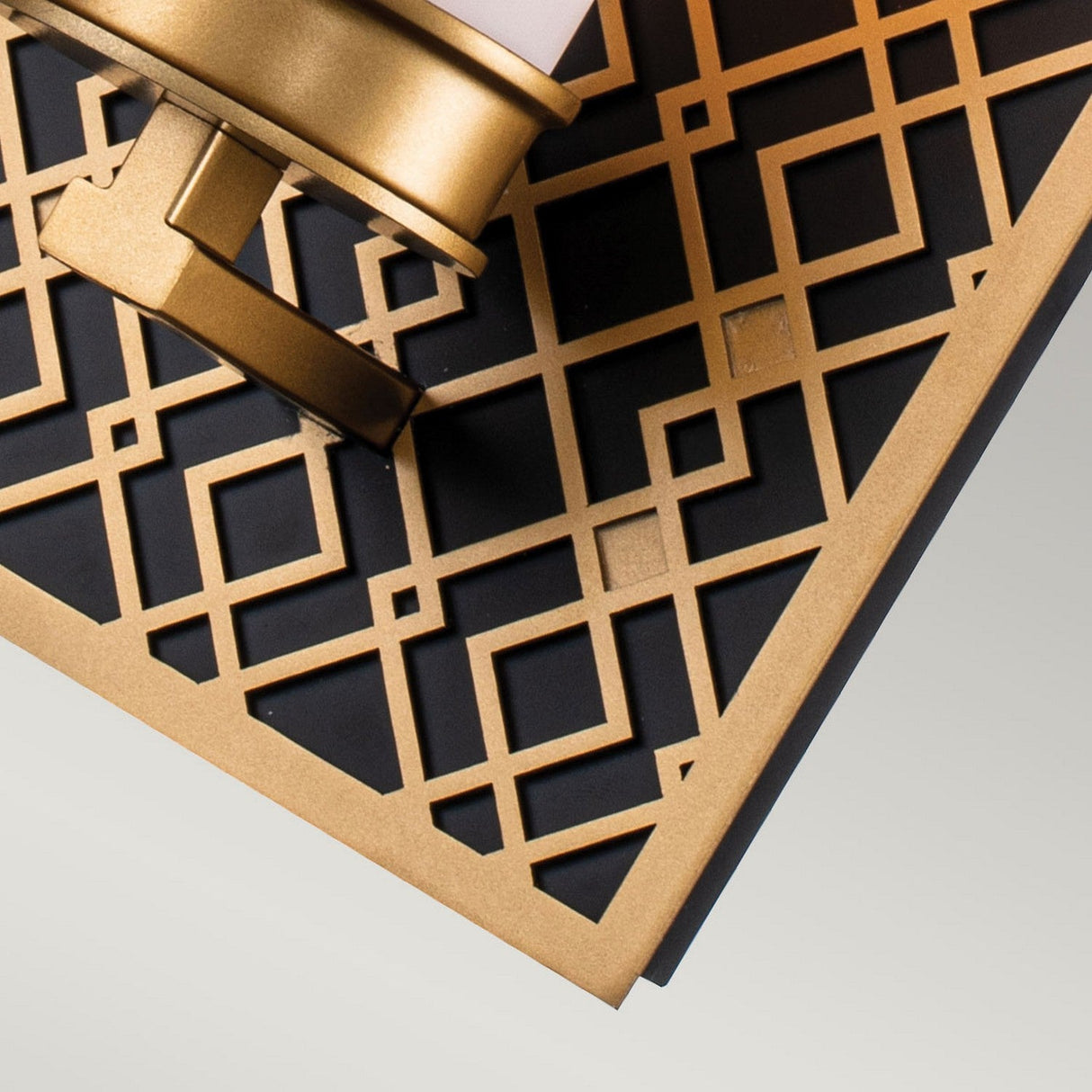 Close-up of a gold geometric wall decor piece set against a black background, showcasing an intricate lattice pattern and a metallic holder extending from the corner, embodying modern design reminiscent of the Ziggy 1 Light Wall Light - Lacquered Gold.