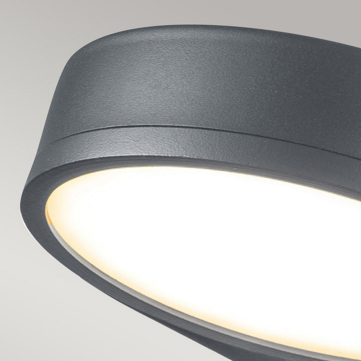 Close-up of the Zola Outdoor LED Wall Light in grey, showcasing its circular design crafted from weather-resistant stainless steel. The light emits a soft, warm glow against a neutral background, making it an ideal choice for enhancing any contemporary space.