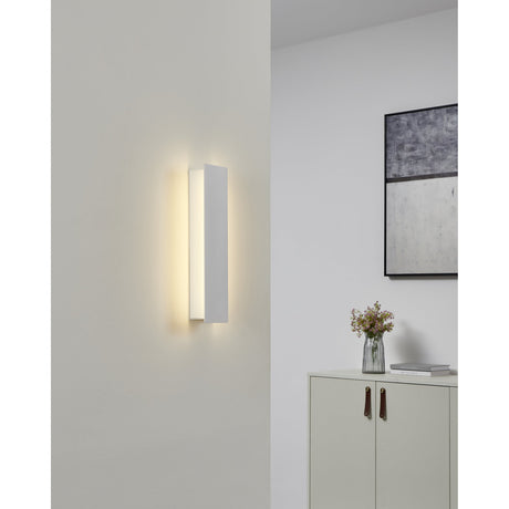 Zubialde LED Wall Light in white aluminium and steel, slim rectangular design with soft uplight glow, mounted on a hallway wall near a console table.